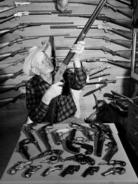 C.J. Hurst of West Covina, Calif., holds up a .44-caliber rimfire Model 66 Winchester rifle as he poses with his collection of about 600 antique guns in 1952.